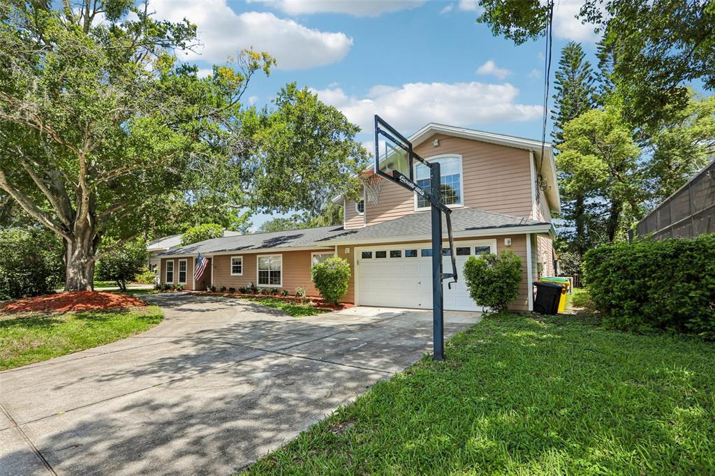 A two-story house with tan siding, a concrete driveway, and a basketball hoop in front — 3131 N CANAL DRIVE, PALM HARBOR, FL
