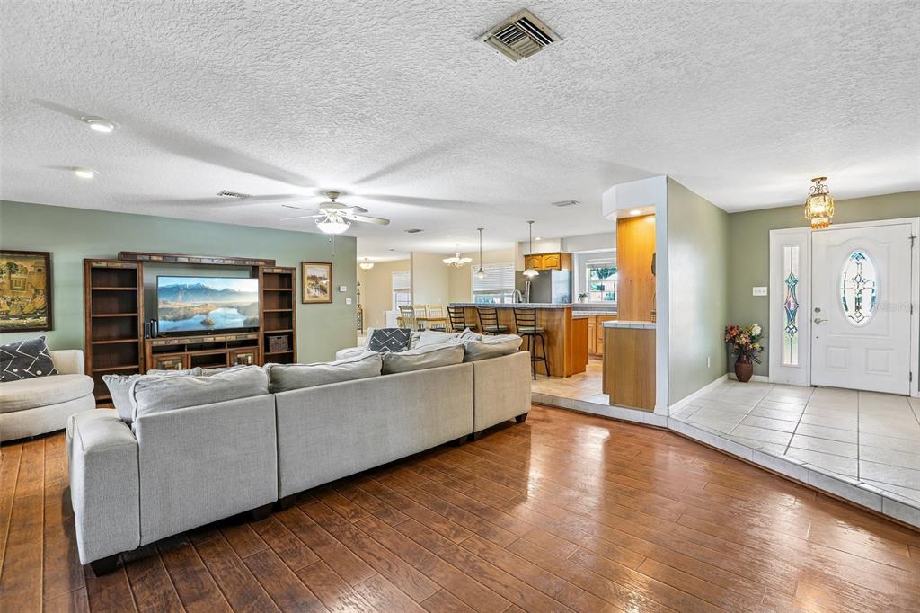 A living room with wood floors, a large sectional sofa, and an open-concept kitchen — 3131 N CANAL DRIVE, PALM HARBOR, FL