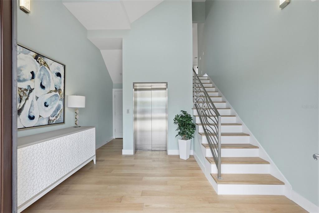 A modern entryway features light wood flooring, a staircase with metal railings, and a home elevator — 15908 GULF BOULEVARD, REDINGTON BEACH, FL