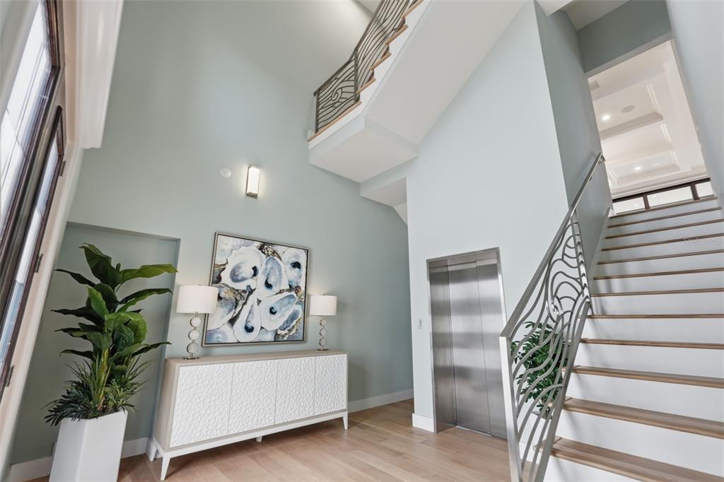 A bright foyer features a staircase with metal railings, a modern elevator, and light wood flooring — 15908 GULF BOULEVARD, REDINGTON BEACH, FL