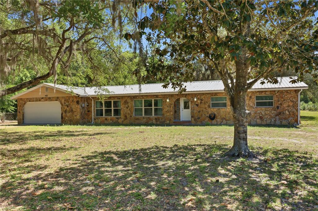 A single-story house with a stone exterior, metal roof, and attached garage under large trees — 67 COVE ROAD, INGLIS, FL