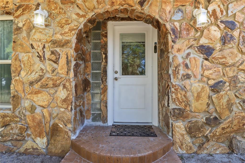 A white front door with a glass pane is set within a stone-clad arched entryway — 67 COVE ROAD, INGLIS, FL