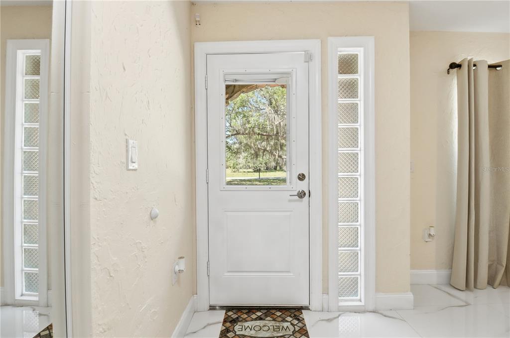 An entryway features a white door with a glass insert, glass block side windows, and tile flooring — 67 COVE ROAD, INGLIS, FL