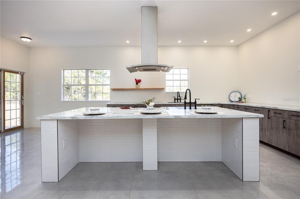 A modern kitchen features a large white marble island, dark wood cabinets, and a stainless hood — 12456 155TH PLACE, LIVE OAK, FL