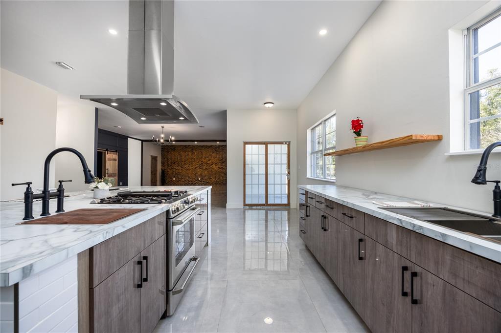 A modern kitchen features wood-grain cabinets, marble countertops, stainless steel appliances, and a brick accent wall — 12456 155TH PLACE, LIVE OAK, FL