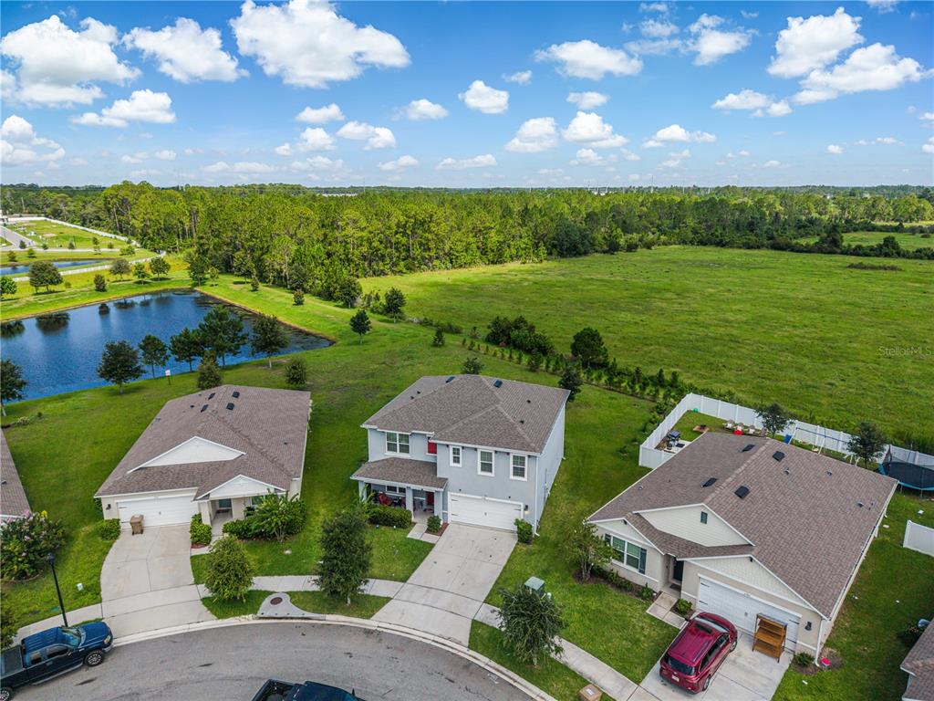 An aerial view shows three suburban houses with driveways, a pond, and a large grassy field — 2786 HARMONIA HAMMOCK ROAD, ST CLOUD, FL