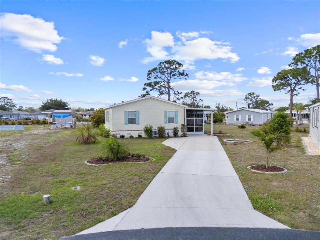 A light yellow manufactured home with a concrete driveway and a screened-in front porch — 9182 PINEHAVEN WAY, ENGLEWOOD, FL