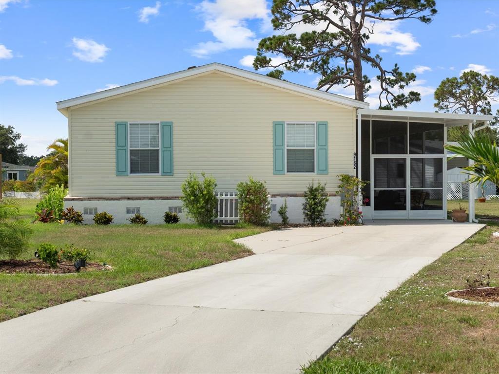 A light yellow manufactured home features a concrete driveway and a screened-in front porch — 9182 PINEHAVEN WAY, ENGLEWOOD, FL