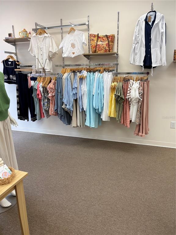 A retail clothing store features wall-mounted racks displaying various garments and a wooden display table — 301 W BAY DRIVE UNIT 5, LARGO, FL