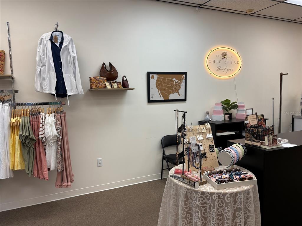 A retail boutique features clothing racks, a display table with accessories, and a wall sign — 301 W BAY DRIVE UNIT 5, LARGO, FL