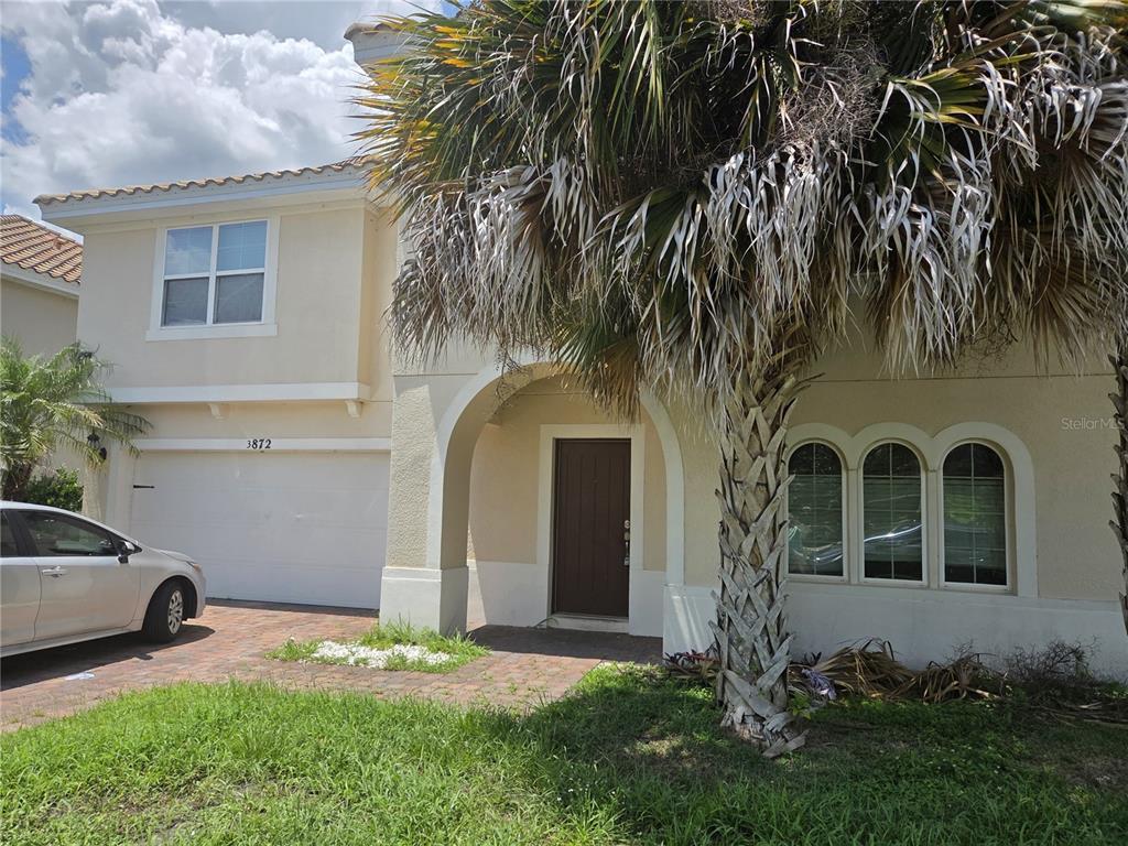 A two-story stucco house features a palm tree, a garage, and an arched entryway — 3872 CARRICK BEND DRIVE, KISSIMMEE, FL