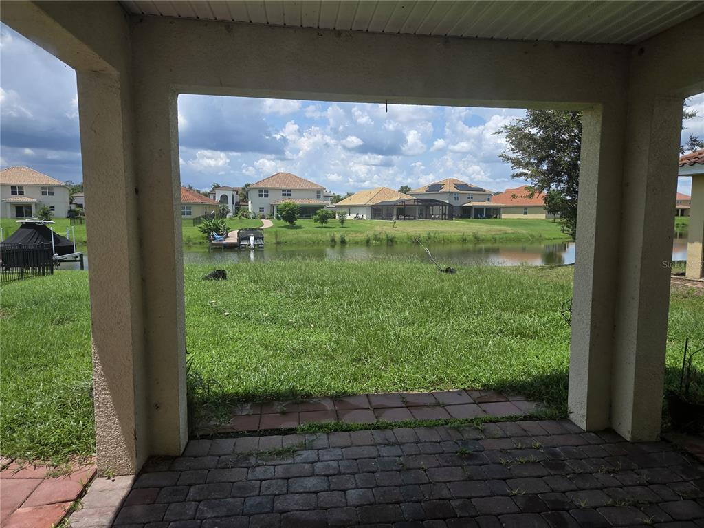 A covered patio overlooks a grassy backyard and a small pond with houses in the distance — 3872 CARRICK BEND DRIVE, KISSIMMEE, FL