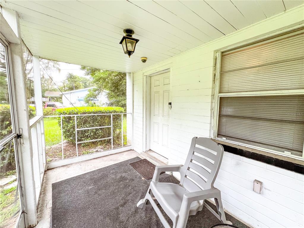 A screened-in porch features a white door, a plastic chair, and a concrete floor — 626 NW 31ST PLACE, GAINESVILLE, FL