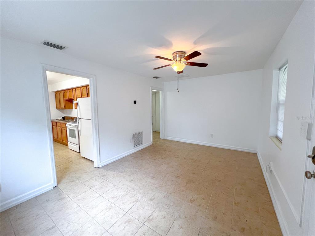 A room with light-colored tile flooring, a ceiling fan, and a doorway leading to a kitchen — 626 NW 31ST PLACE, GAINESVILLE, FL