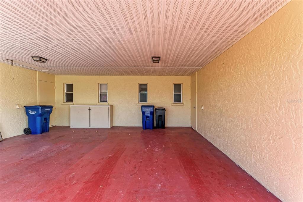 A covered carport with a red concrete floor, yellow stucco walls, and four small windows — 390 301 BOULEVARD W UNIT 8C, BRADENTON, FL
