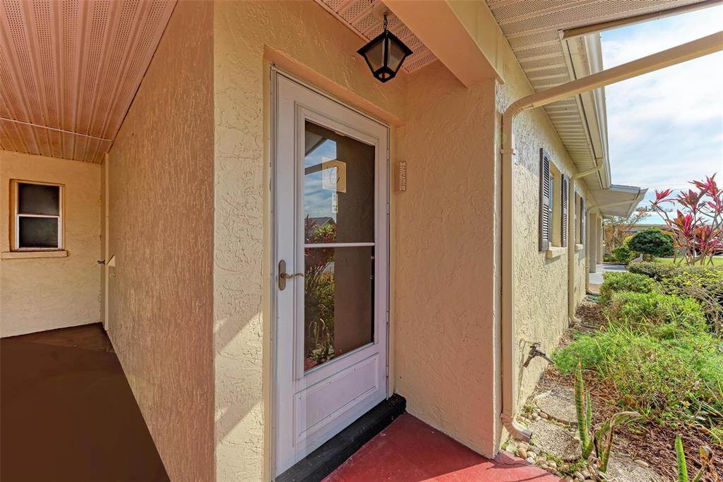 A white storm door leads into a home entrance with a covered porch and landscaping — 390 301 BOULEVARD W UNIT 8C, BRADENTON, FL