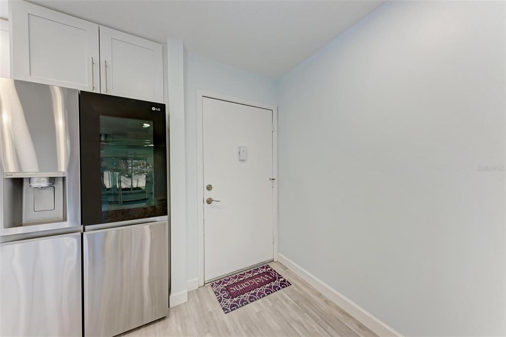 A stainless steel refrigerator stands next to a white door in a light-walled room — 390 301 BOULEVARD W UNIT 8C, BRADENTON, FL