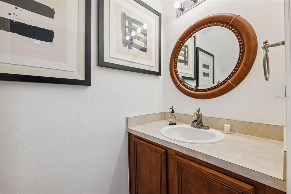 A powder room features a wooden vanity, a round mirror, and framed abstract wall art — 12224 FOXMOOR PEAK DRIVE, RIVERVIEW, FL