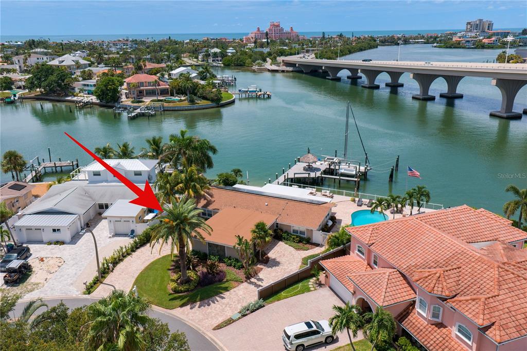 An aerial view shows a waterfront house with a pool, palm trees, and a bridge — 3142 W VINA DEL MAR BOULEVARD, ST PETE BEACH, FL