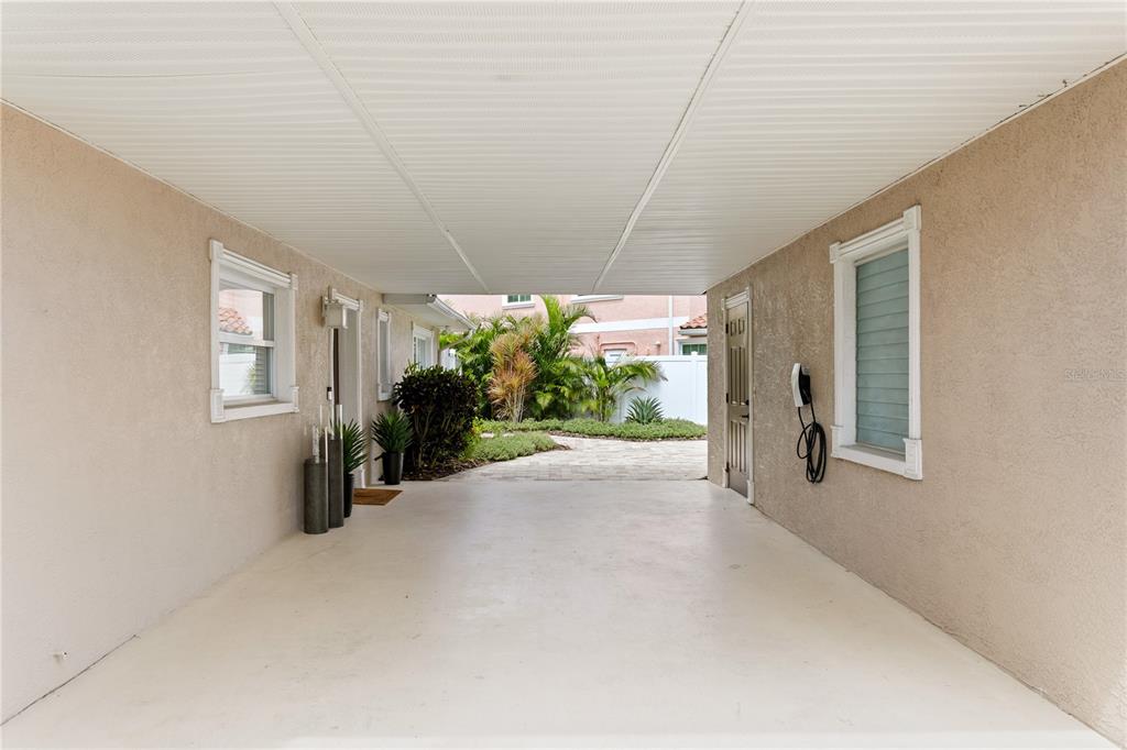 A covered carport features beige stucco walls, a white ceiling, and an electric vehicle charger — 3142 W VINA DEL MAR BOULEVARD, ST PETE BEACH, FL