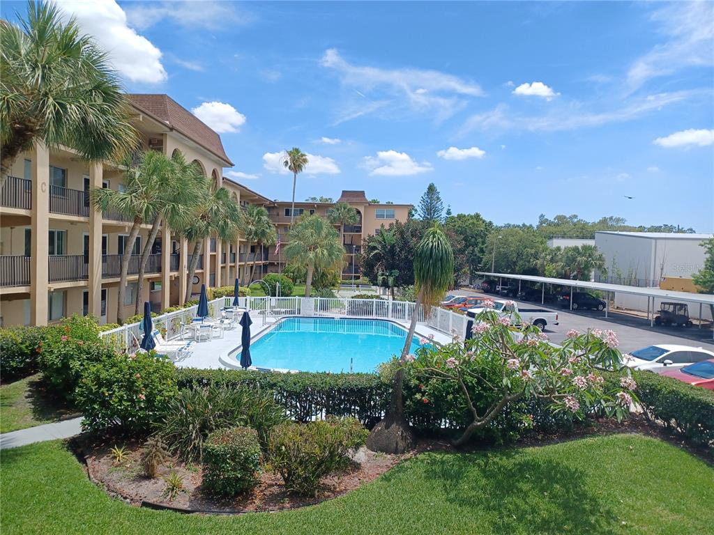 A swimming pool sits in the courtyard of a multi-story apartment complex with palm trees — 2525 W BAY DRIVE UNIT A12, BELLEAIR BLUFFS, FL