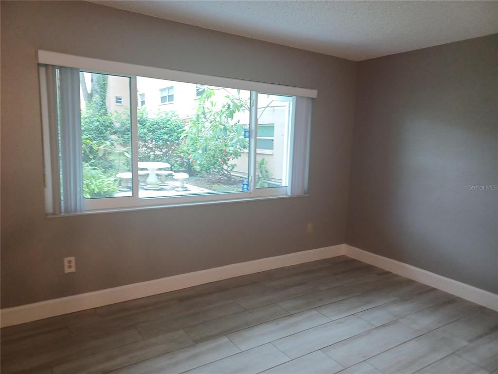 An empty room features gray walls, light wood-look flooring, and a large window overlooking a patio — 2525 W BAY DRIVE UNIT A12, BELLEAIR BLUFFS, FL