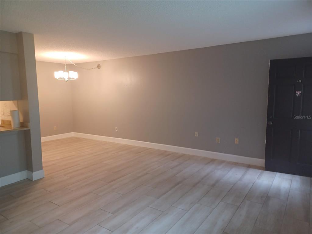 An empty room with light wood-look tile flooring, gray walls, and a dark entry door — 2525 W BAY DRIVE UNIT A12, BELLEAIR BLUFFS, FL