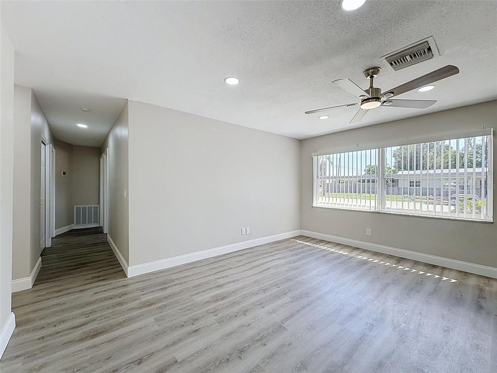 An empty room features light gray walls, wood-look flooring, a ceiling fan, and large windows — 14998 MOCKINGBIRD LANE, CLEARWATER, FL