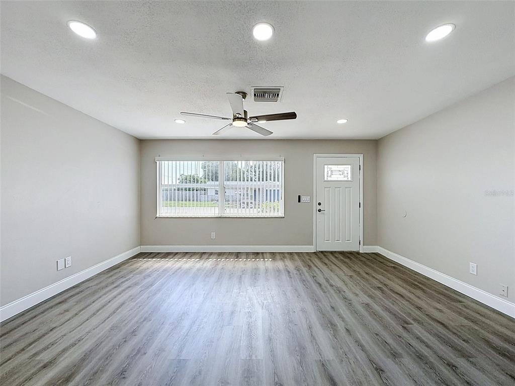 An empty room features light gray walls, wood-look flooring, a ceiling fan, and a white door — 14998 MOCKINGBIRD LANE, CLEARWATER, FL