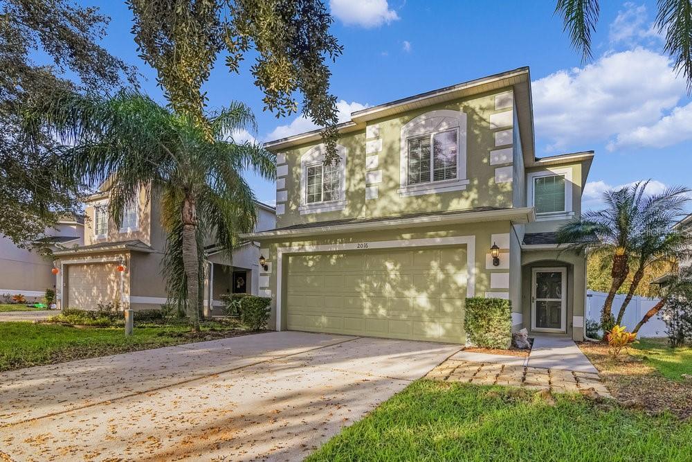 A two-story house with light green stucco siding, a two-car garage, and a palm tree — 2016 PORTCASTLE CIRCLE, WINTER GARDEN, FL