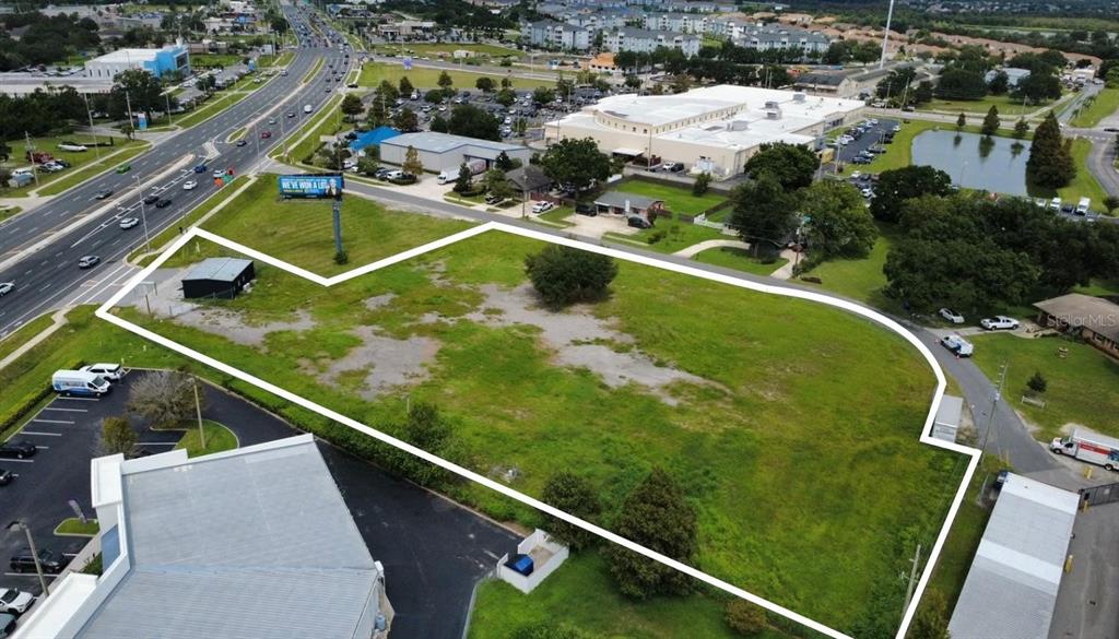 An aerial view shows a vacant, grassy lot outlined in white next to a busy road — 2543 E IRLO BRONSON MEMORIAL HIGHWAY, KISSIMMEE, FL