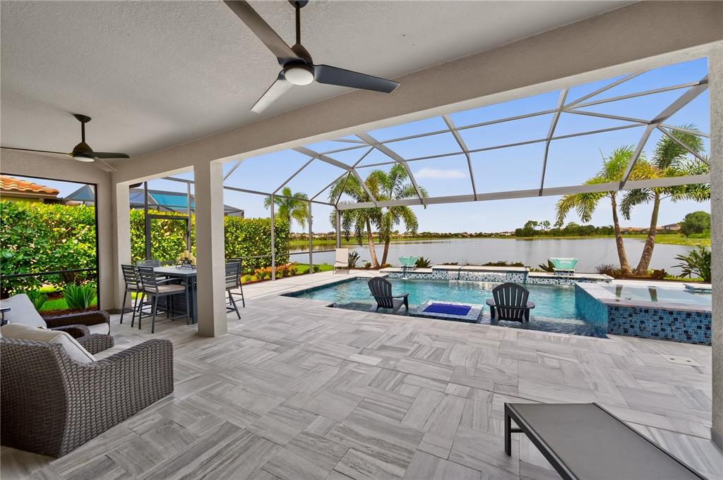 A covered patio overlooks a swimming pool and a lake enclosed by a screen cage — 17618 POLO TRAIL, BRADENTON, FL