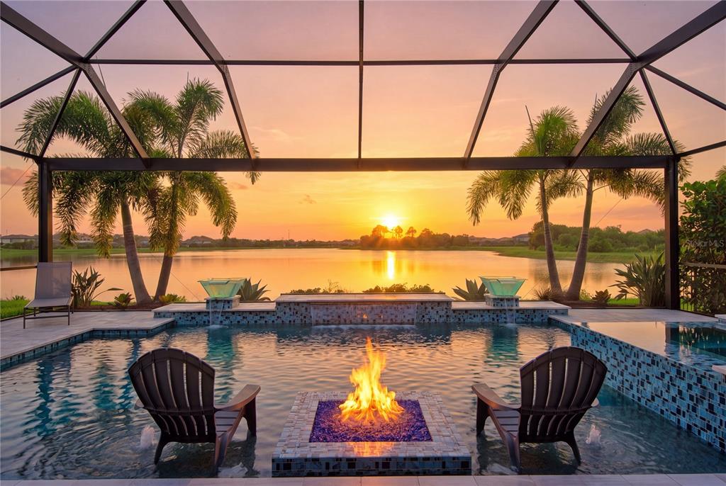 A swimming pool with a central fire pit and water features overlooks a lake at sunset — 17618 POLO TRAIL, BRADENTON, FL