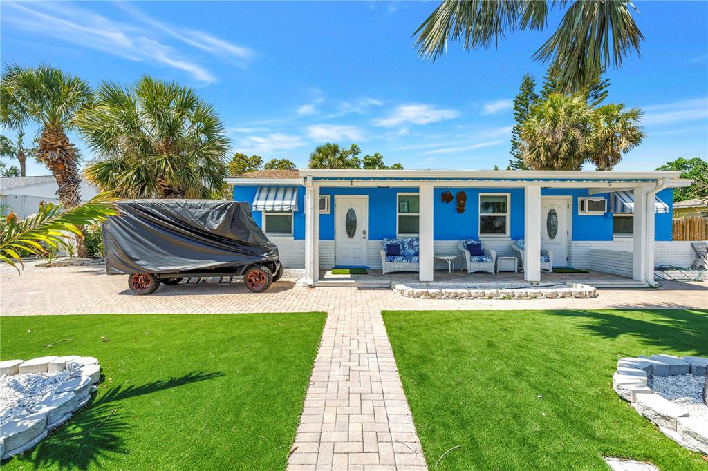 A bright blue single-story house with a covered porch, brick walkway, and artificial grass lawn — 6892 GULF WINDS DRIVE UNIT 2, ST PETE BEACH, FL