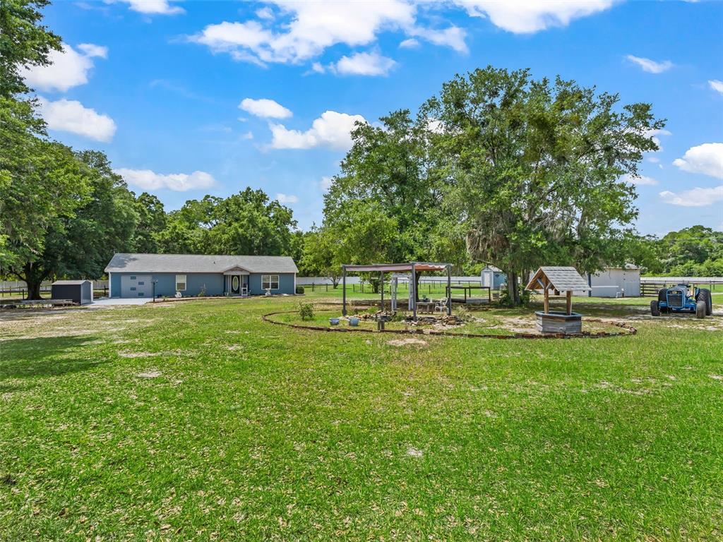 A blue house sits on a grassy lot with a wishing well and large trees — 967 E HIGHWAY 316, CITRA, FL