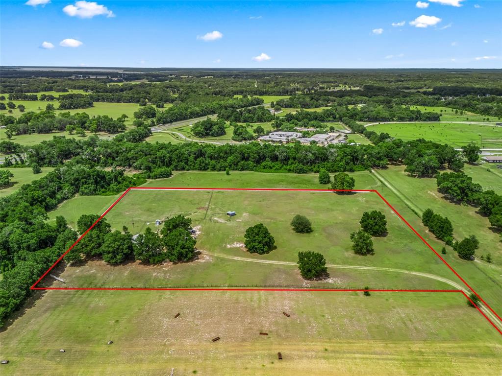 An aerial view shows a large, fenced-in grassy pasture with scattered trees and small structures — 967 E HIGHWAY 316, CITRA, FL