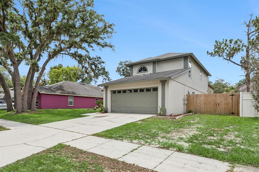 A two-story house with a beige stucco exterior, a gray garage door, and a wooden fence — 4017 QUAIL BRIAR DRIVE, VALRICO, FL