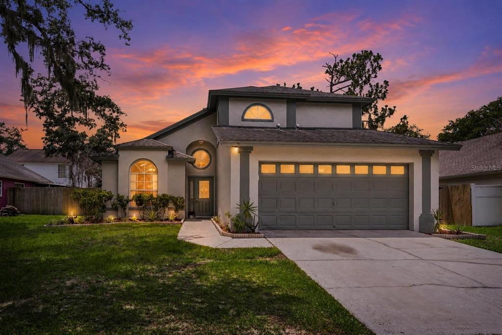 A two-story house with a gray garage, arched windows, and a sunset sky background — 4017 QUAIL BRIAR DRIVE, VALRICO, FL