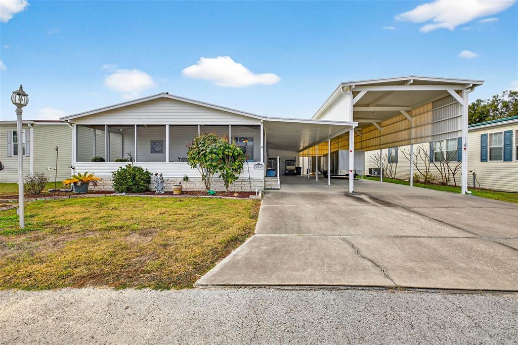 A single-story manufactured home features a screened-in porch, a concrete driveway, and a metal carport — 10047 EQUITY AVENUE, DADE CITY, FL