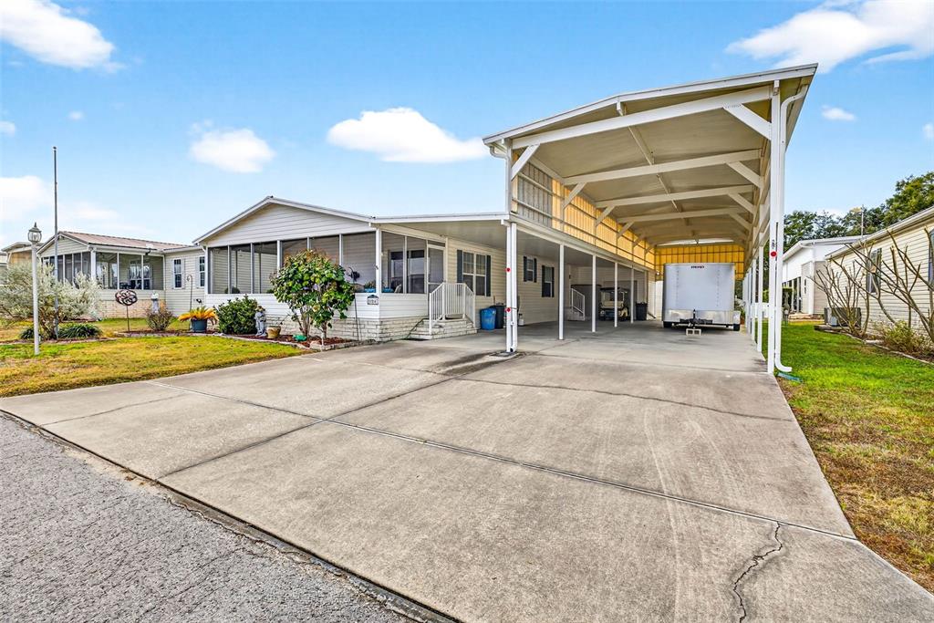 A single-story manufactured home features a large concrete driveway and an attached metal carport — 10047 EQUITY AVENUE, DADE CITY, FL