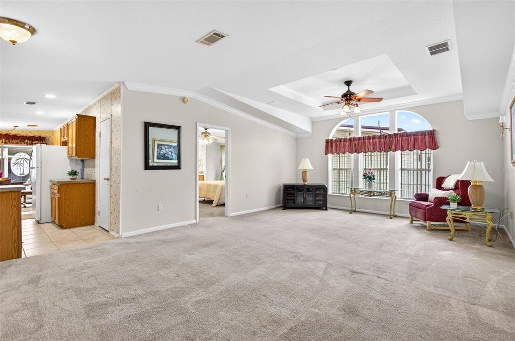 A spacious living room with beige carpet, a tray ceiling, and large arched windows — 10047 EQUITY AVENUE, DADE CITY, FL