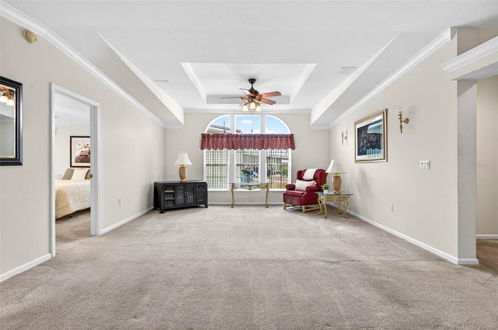 A carpeted living room features a tray ceiling, a ceiling fan, and large arched windows — 10047 EQUITY AVENUE, DADE CITY, FL