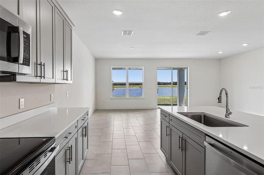 A modern kitchen features gray cabinets, white countertops, a center island, and a water view — 5030 SALADO DRIVE, ST CLOUD, FL