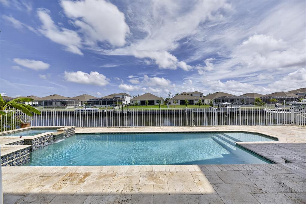 A backyard swimming pool and spa overlook a canal with houses in the background — 715 ISLEBAY DRIVE, APOLLO BEACH, FL