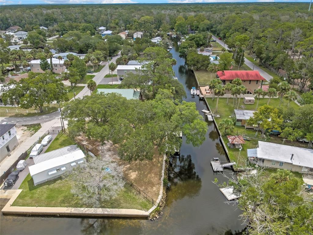 An aerial view shows a canal flowing through a residential neighborhood with houses and trees — 6134 ISLAND DRIVE, WEEKI WACHEE, FL