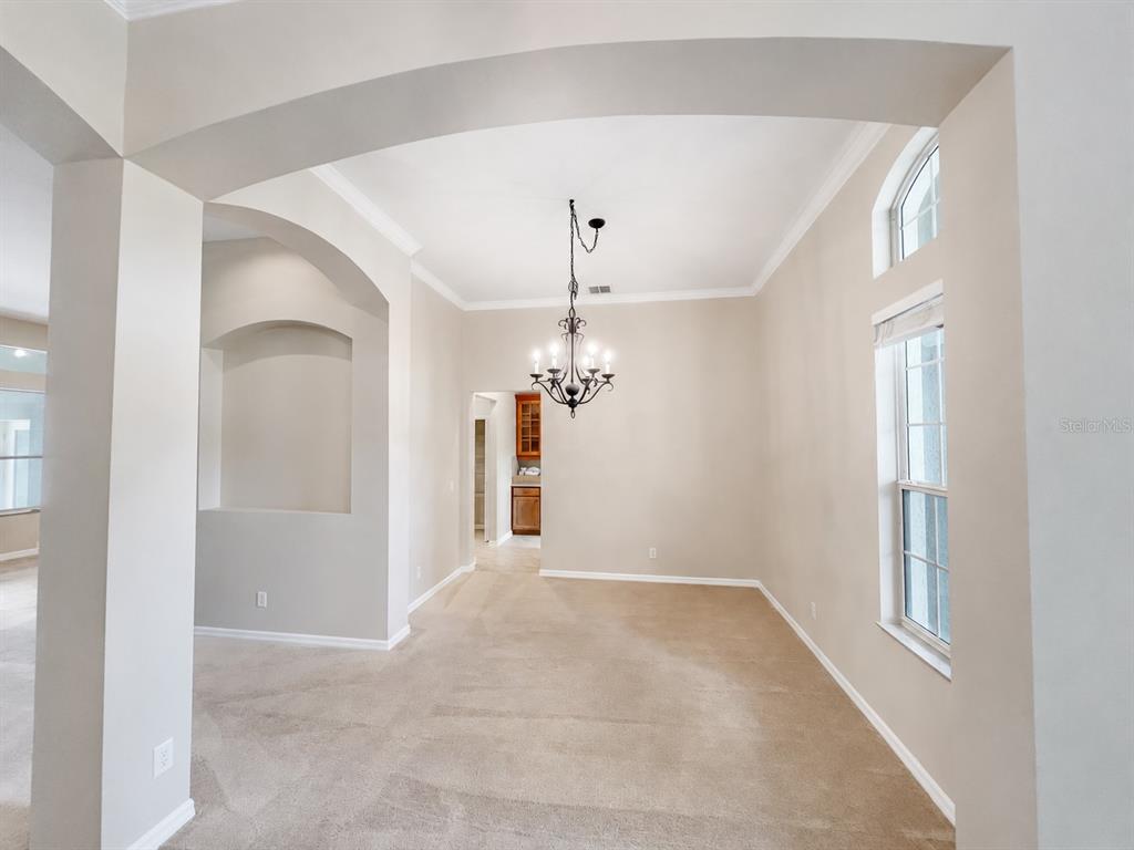 A dining room with beige carpet, a chandelier, arched entryways, and a large window — 105 E BLUE WATER EDGE DRIVE, EUSTIS, FL