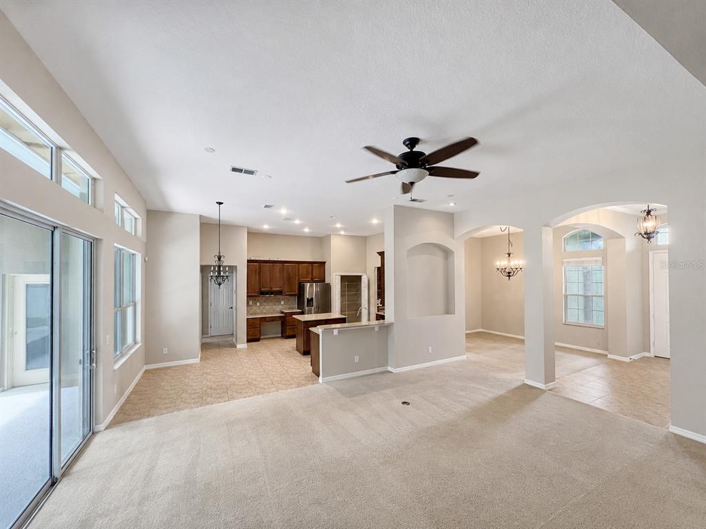 An open-concept living area features carpeted flooring, a kitchen with wood cabinetry, and arched entryways — 105 E BLUE WATER EDGE DRIVE, EUSTIS, FL