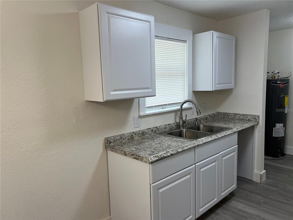 A kitchen features white cabinets, a granite countertop, a double sink, and a water heater — 2075 DIXIE AVENUE, SANFORD, FL