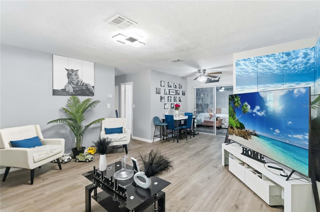 A living room features light wood flooring, a large television, and two white armchairs — 568 E NORMANDY BOULEVARD, DELTONA, FL