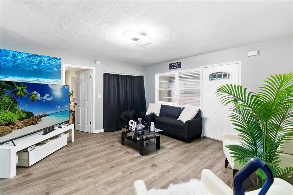 A living room features light wood-look flooring, a black sofa, and a large television — 568 E NORMANDY BOULEVARD, DELTONA, FL